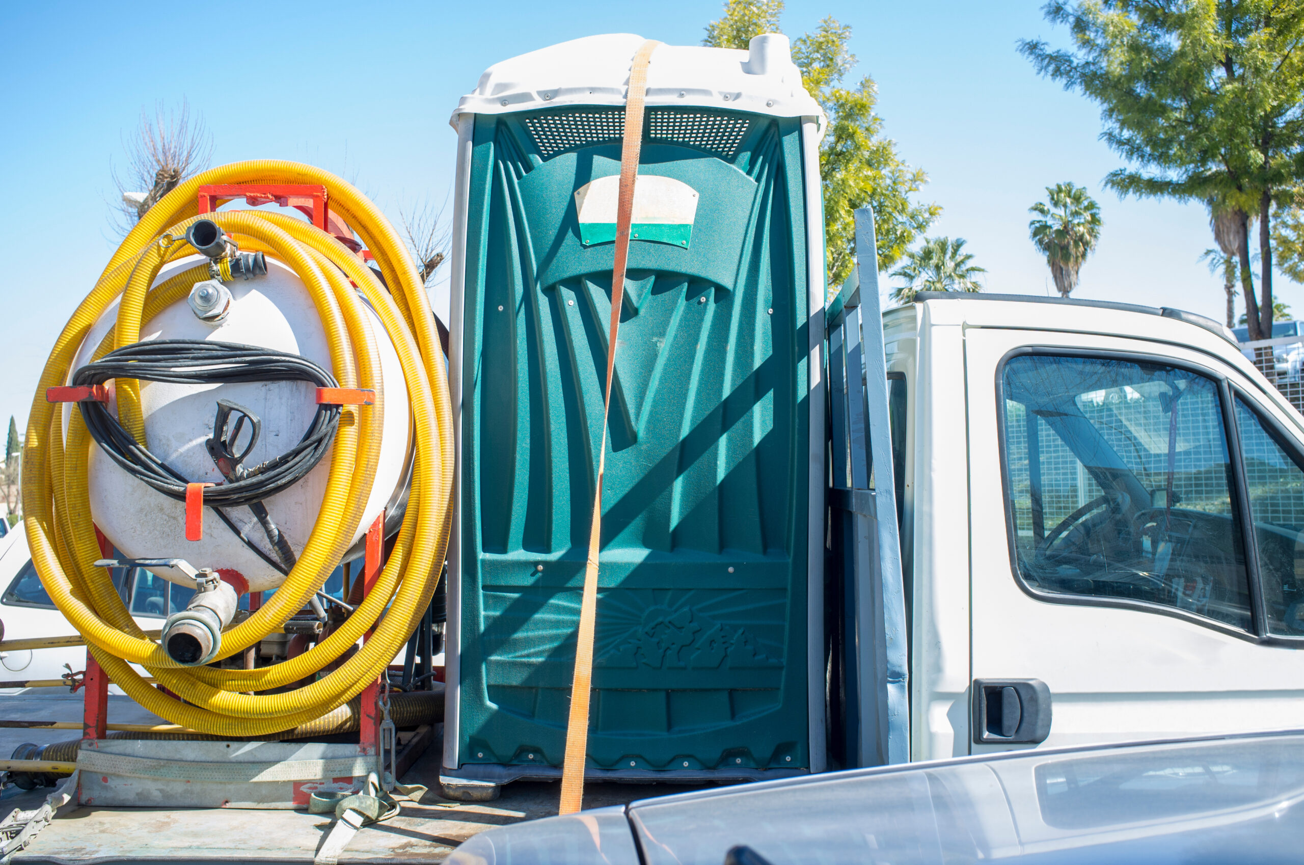 Portable toilet with pump loaded over small truck in a parking lot.