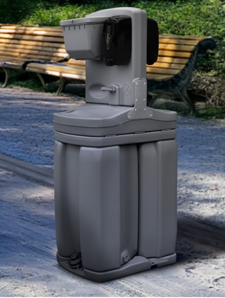 A grey portable handwashing station on the edge of a gravel road.